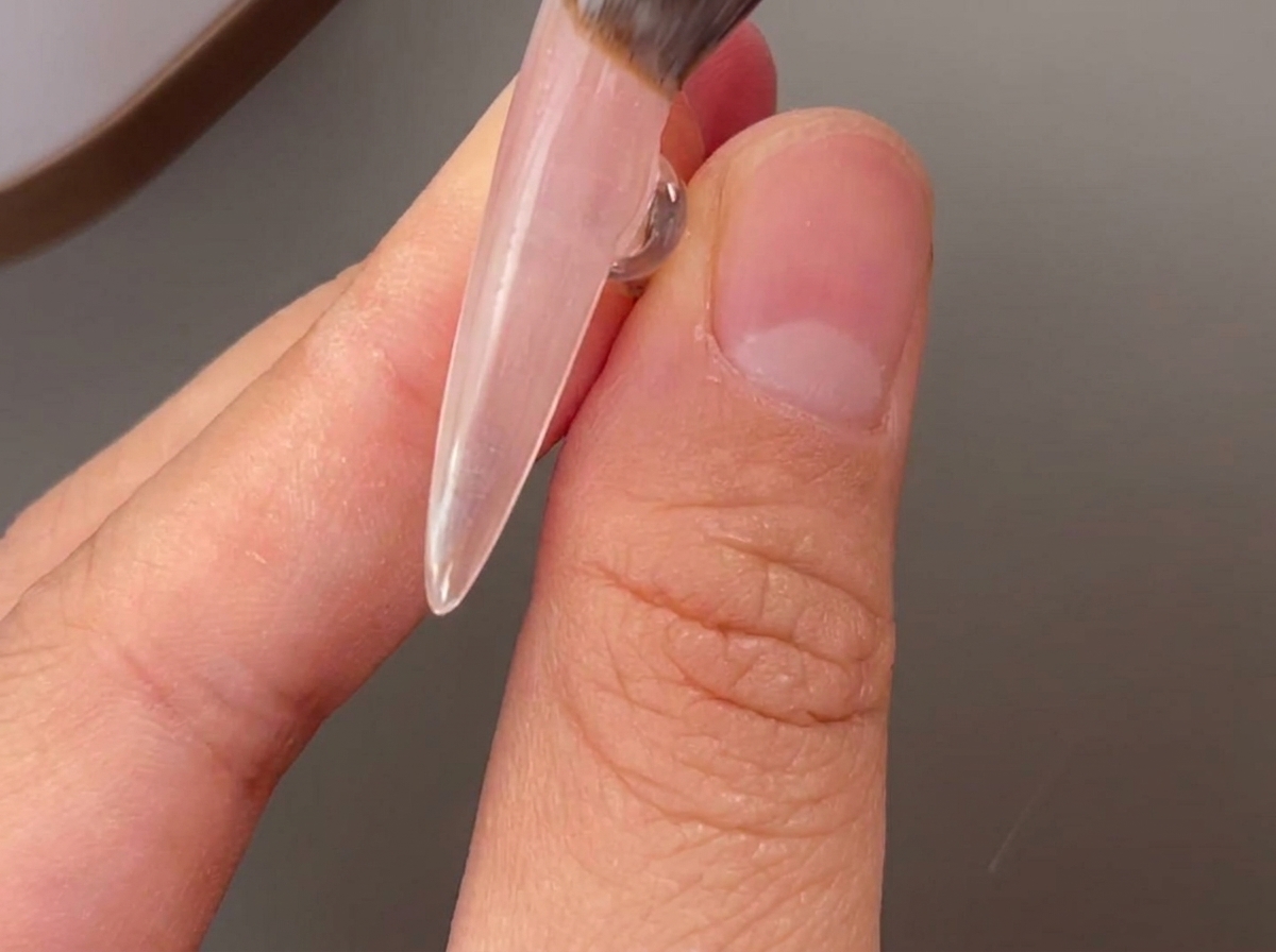 Un pennello applica uno strato di base gel trasparente su ununghia naturale.