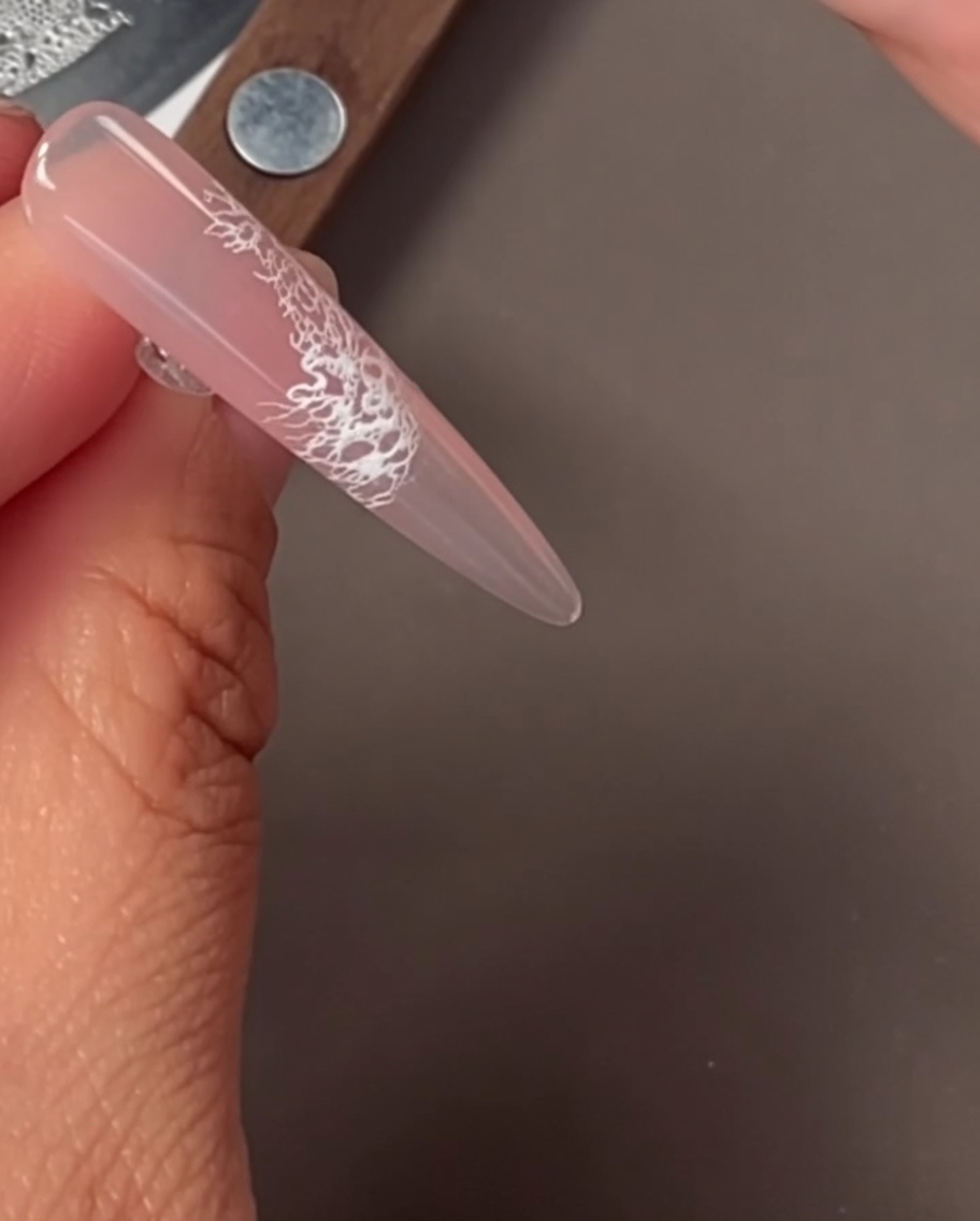 Primo piano di ununghia con un delicato motivo in pizzo bianco applicato tramite stamping.