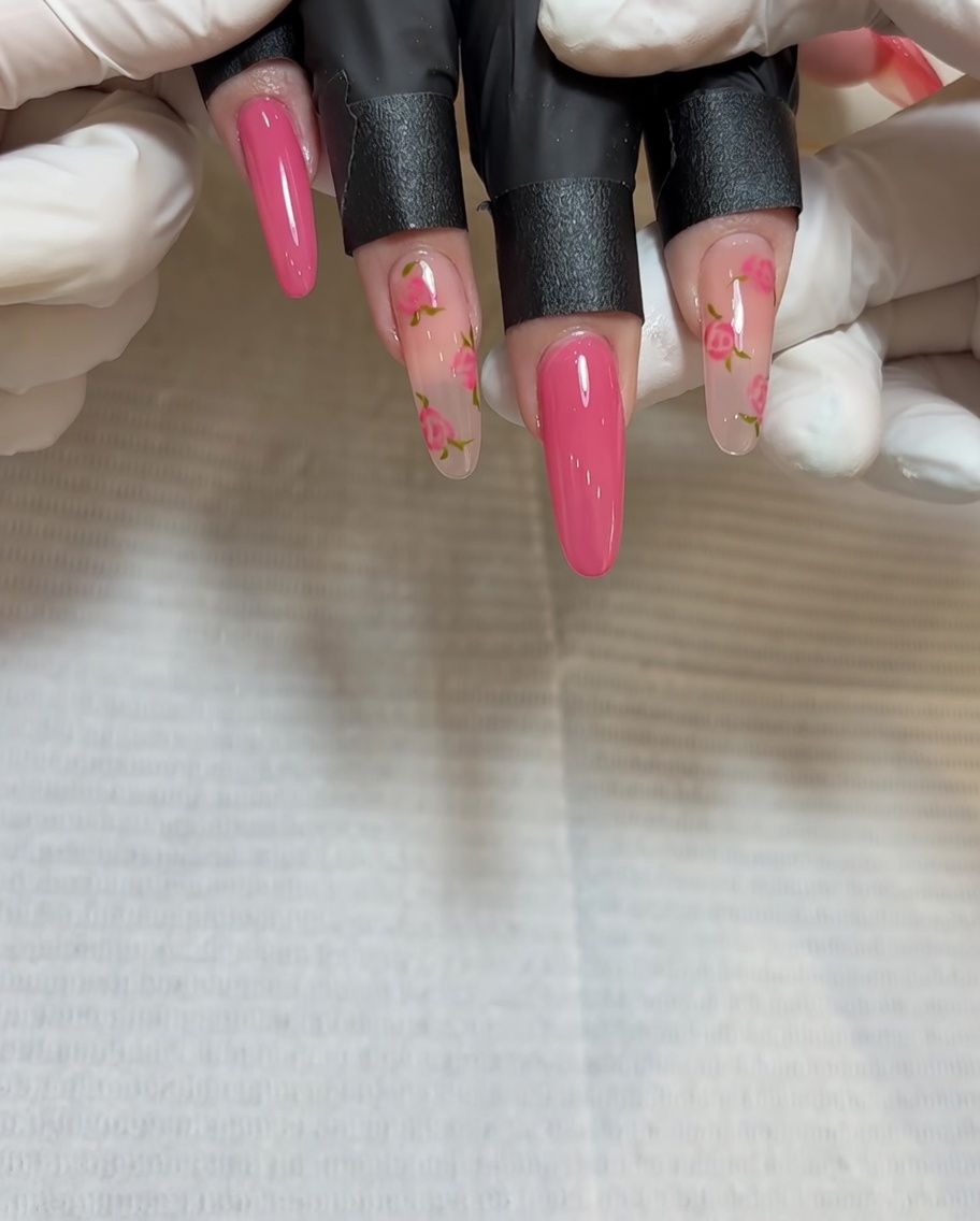Primo piano di un pennello che applica gel rosso più profondo al centro del secondo grappolo di rose sullunghia.