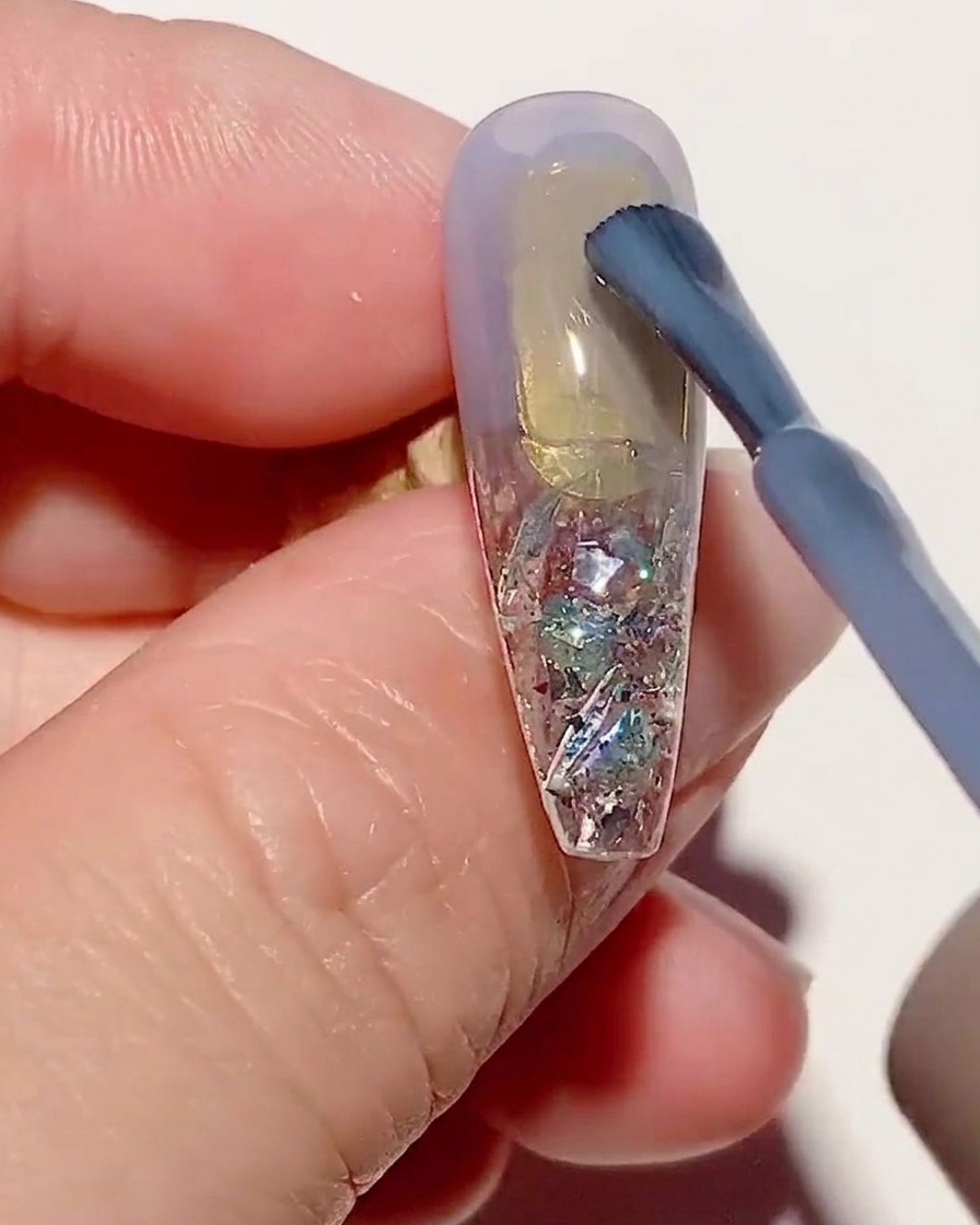 Un pennello applica uno strato sottile di smalto gel blu trasparente su una tip testurizzata.