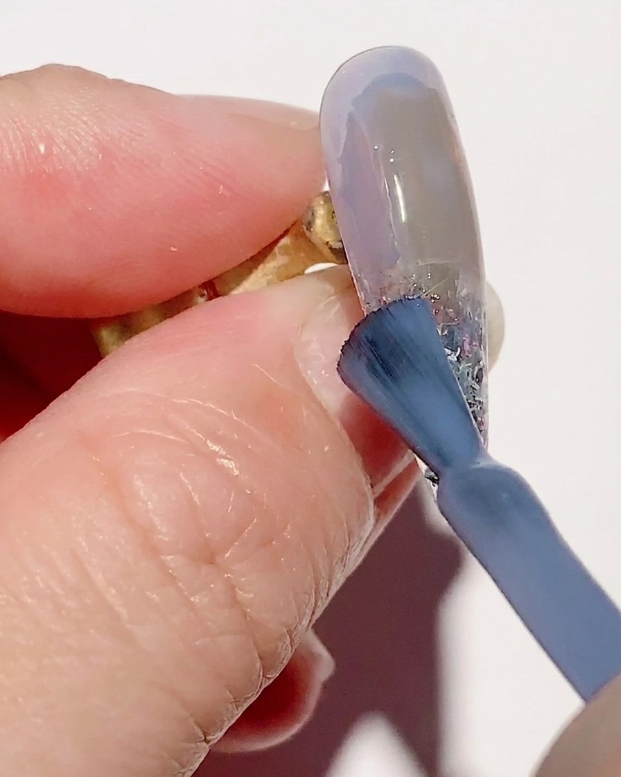 Un pennello per sfumature lavora lo smalto gel blu trasparente sulla superficie dellunghia per una transizione fluida.