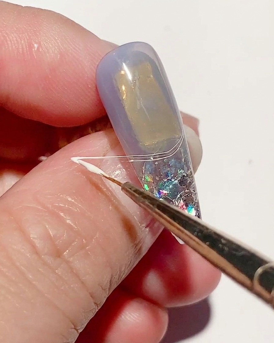 Un pennello sottile stende lo spider gel bianco sulla superficie dellunghia creando linee sottili a ragnatela.