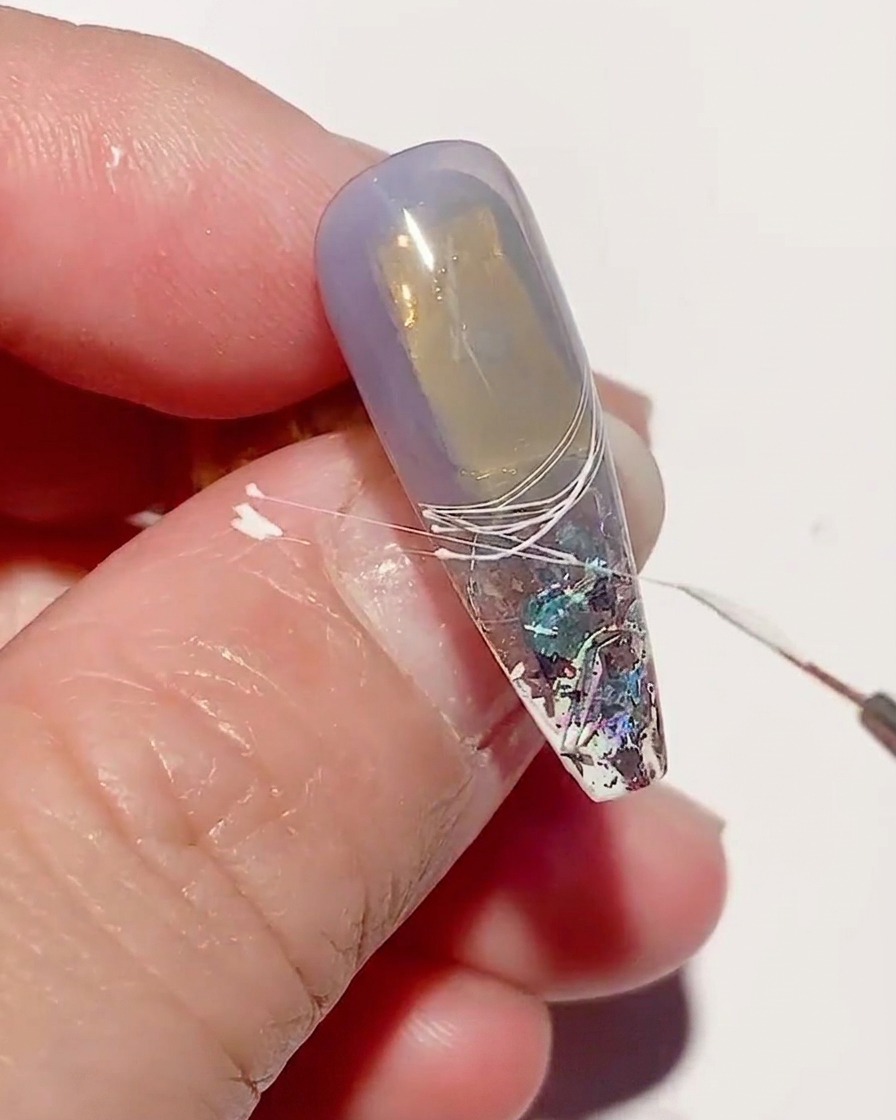 Primo piano di ununghia con linee di spider gel bianco in polimerizzazione sotto una lampada UV.
