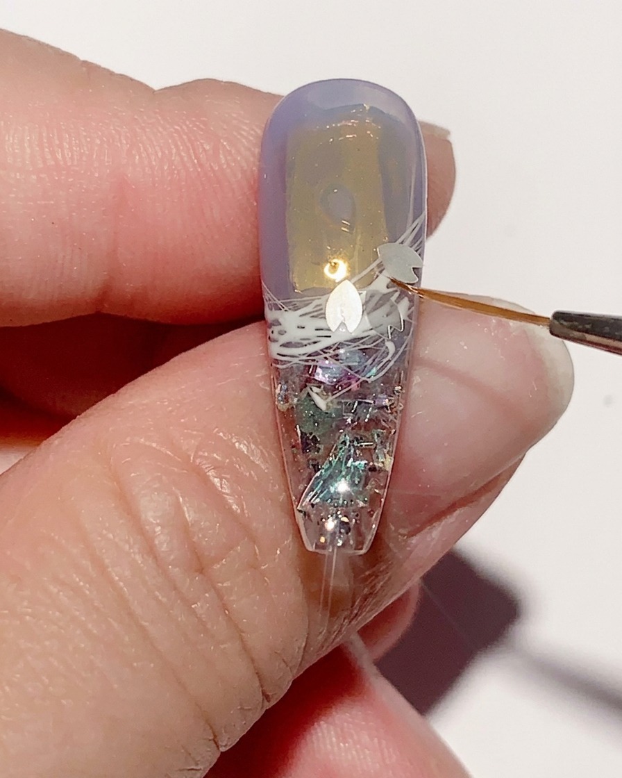 Pinzette posizionano piccole paillettes a forma di fiore di ciliegio sulla superficie umida del gel.