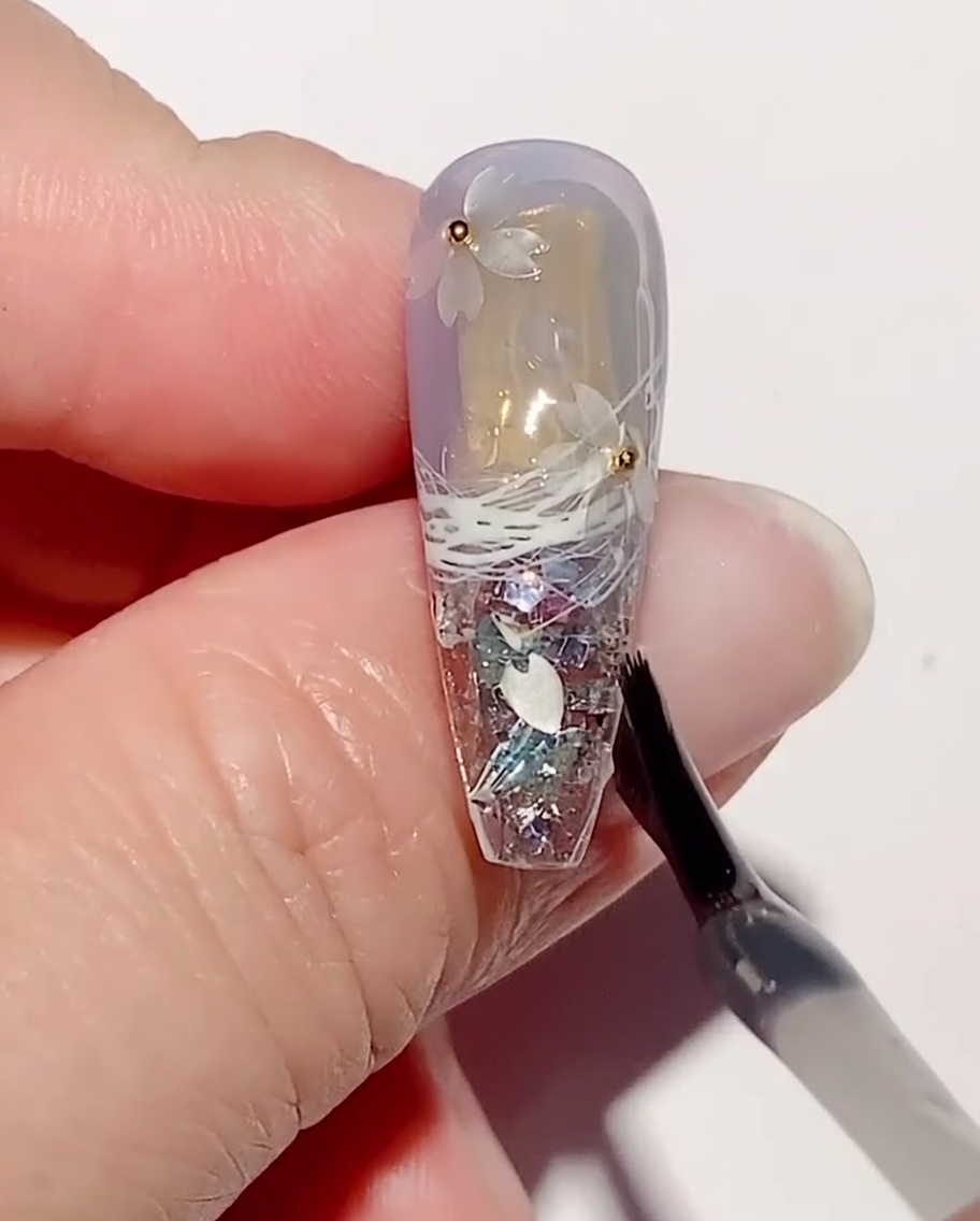 Un pennello applica uno strato di gel di rinforzo trasparente su paillettes e perline.