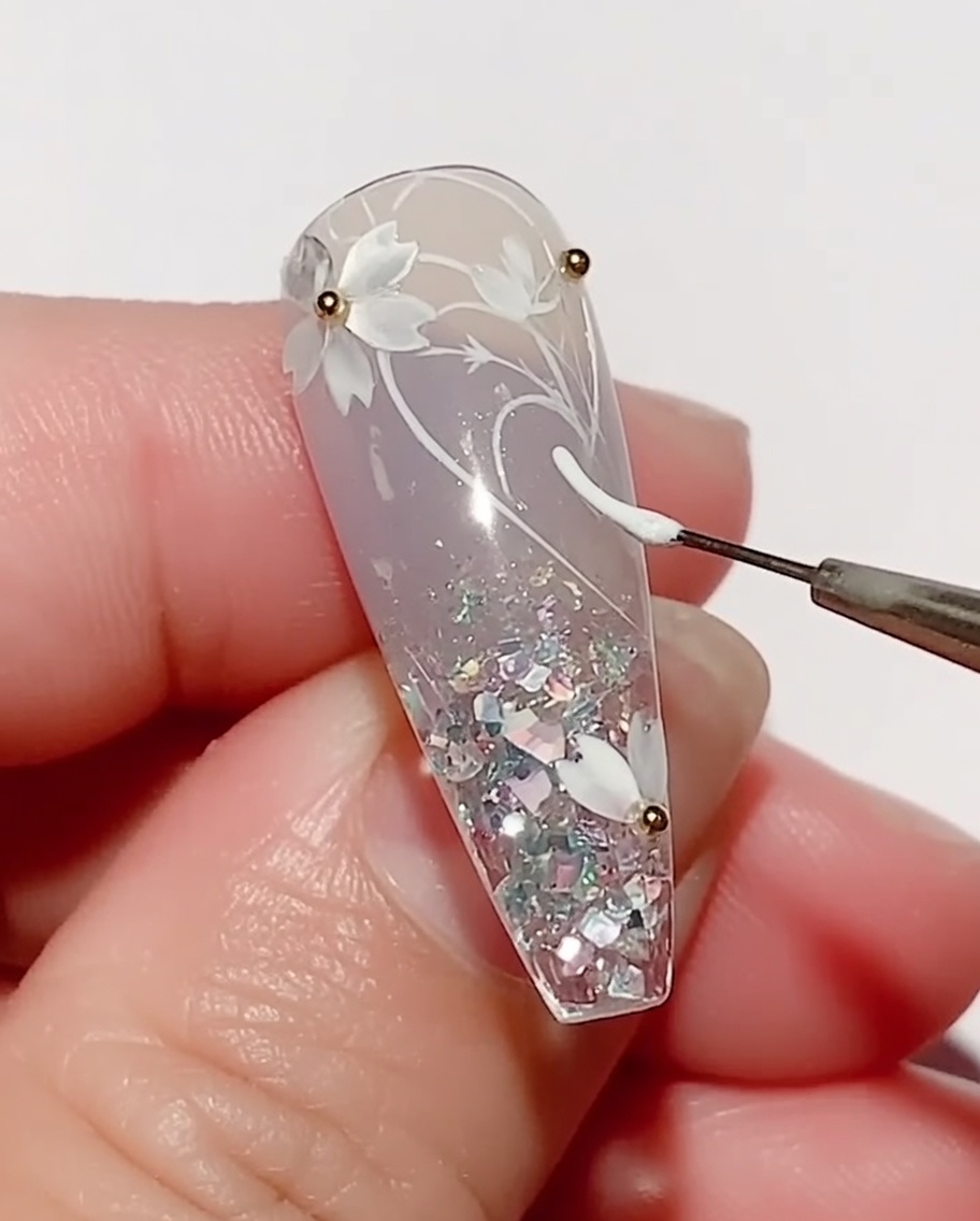 Un pennello sottile applica gel colorato bianco per disegnare la forma di una foglia sullunghia decorata.