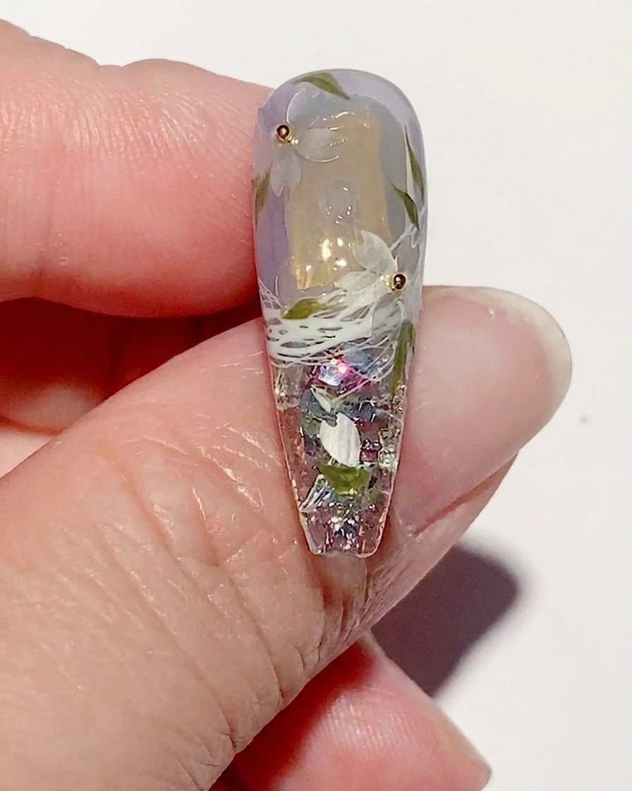 Ununghia decorata con fiori di ciliegio su cui viene applicato un top coat lucido.
