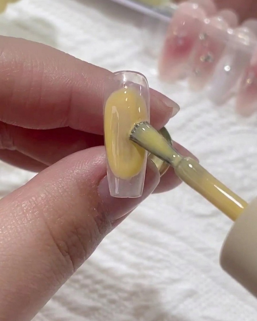 Un pennello applica un sottile strato di base gel trasparente su ununghia naturale.