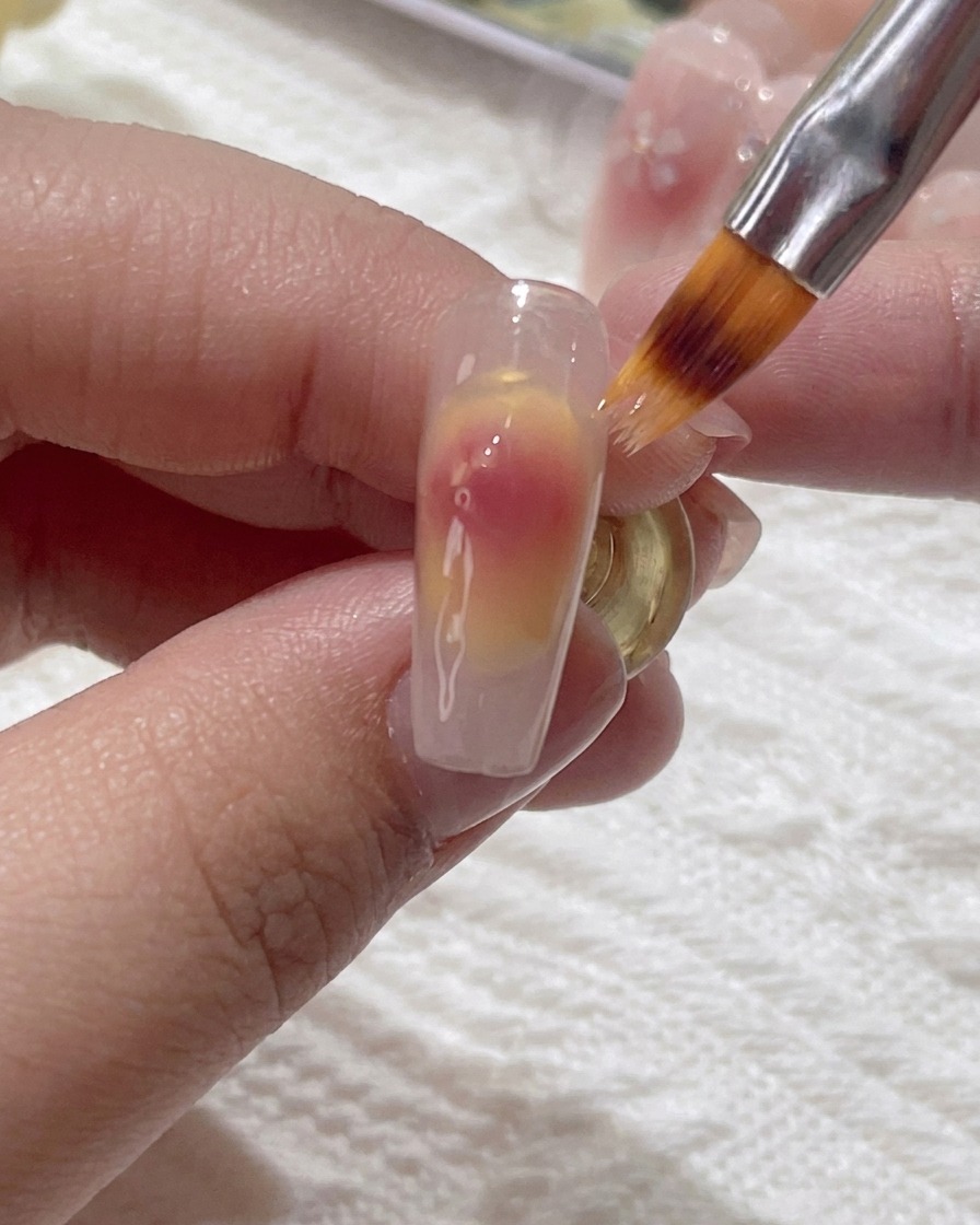 Un piccolo pennello sfuma delicatamente il gel rosa sulla superficie dellunghia.