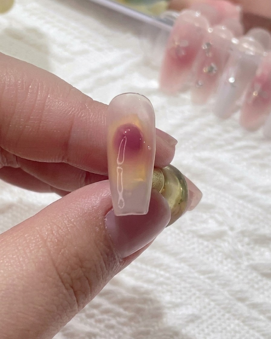 Primo piano di un pennello che sfuma una goccia di gel rosa su ununghia trasparente per creare una sfumatura blush morbida.