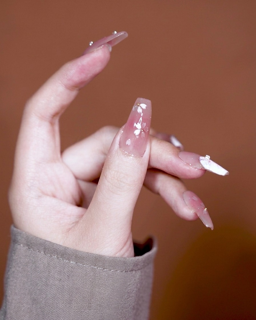 Un pennello applica un gel adesivo spesso e trasparente su ununghia con base sfumata rosa.