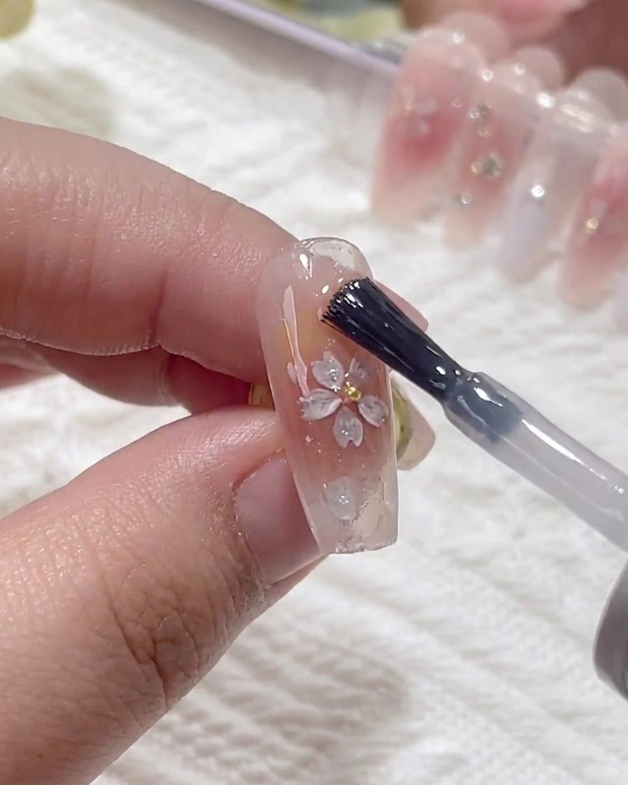 Un pennello applica uno strato di gel costruttore trasparente sopra lunghia, coprendo i fiori applicati.