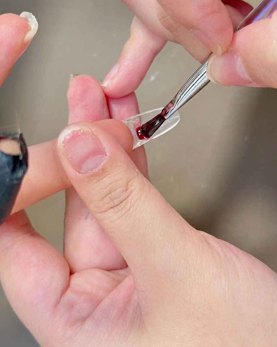 Un pennello che applica uno strato di gel bianco lattiginoso sulla superficie di una tip trasparente.