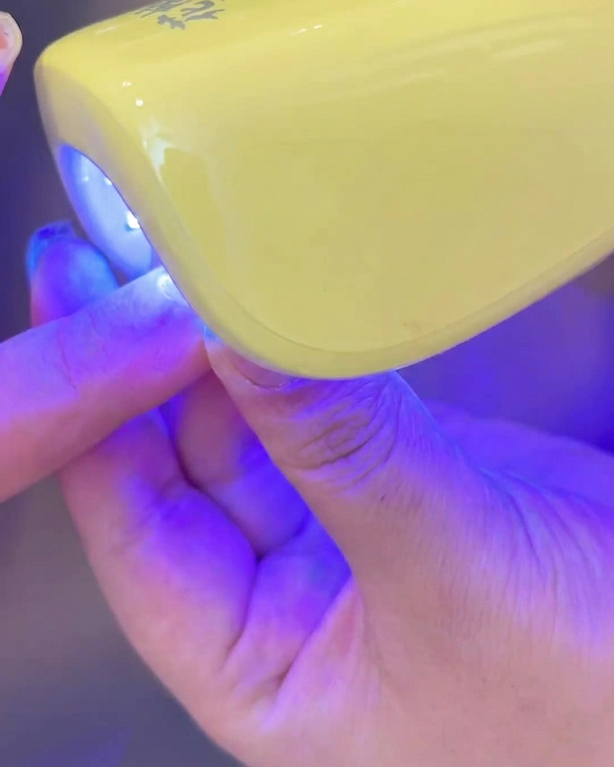 Una mano che inserisce ununghia con gel bianco lattiginoso sotto una lampada UV/LED.