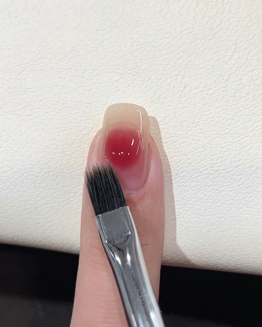 Un pennello piatto per sfumature che ammorbidisce i bordi del punto di gel rosa su ununghia.