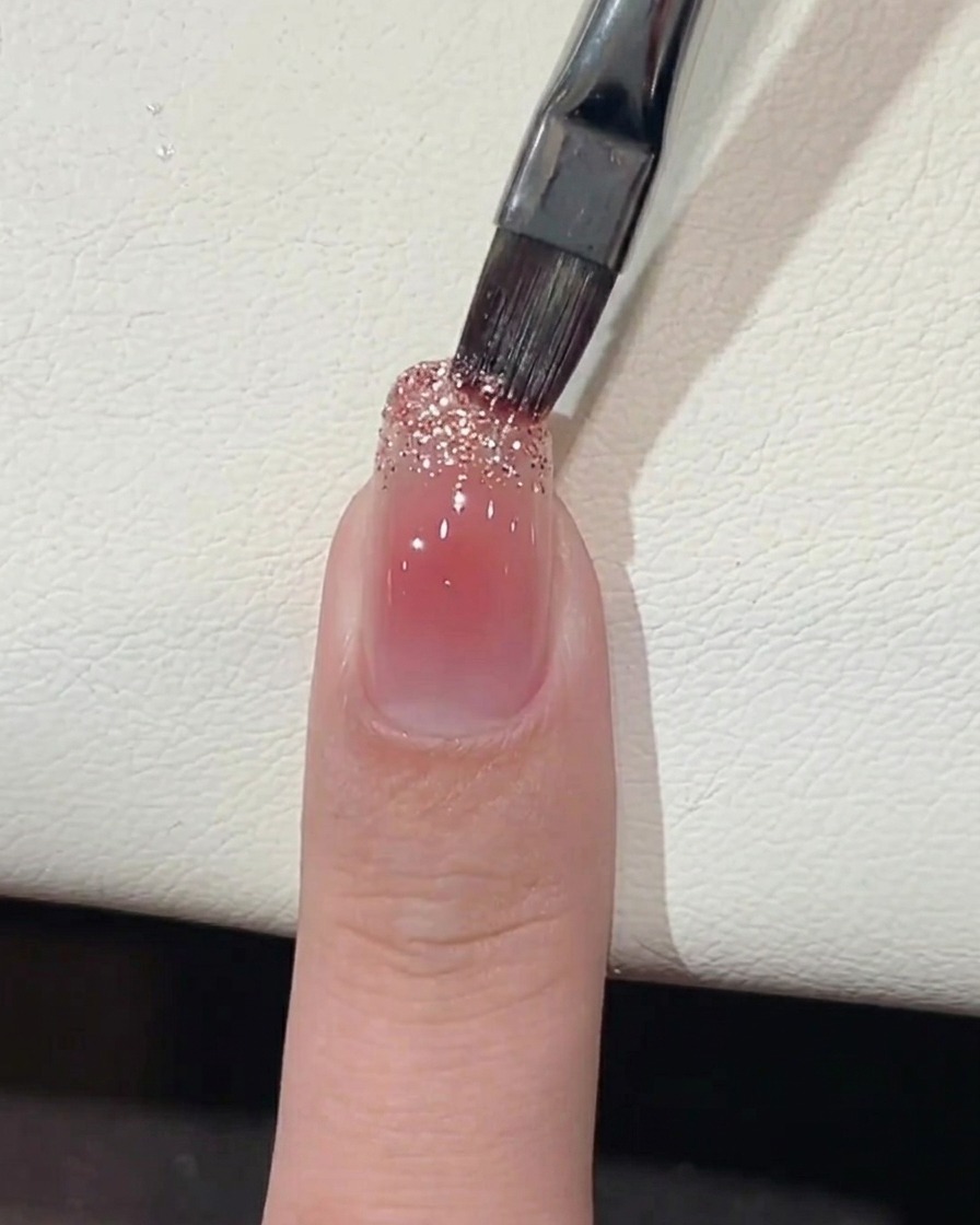 Un pennello che applica gel glitterato a grana grossa sul bordo libero dellunghia.