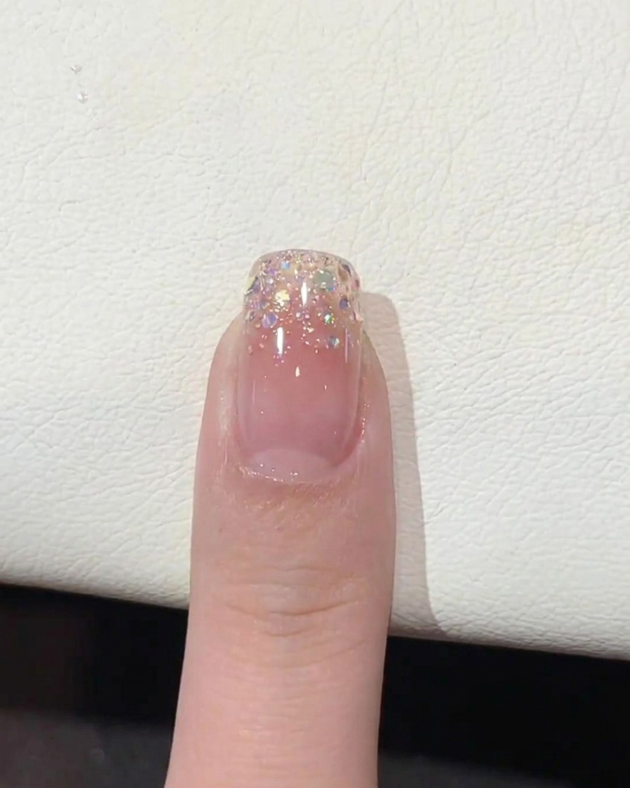 Un pennello che applica un top coat chiaro e lucido sopra la punta dellunghia con sfumatura glitter.