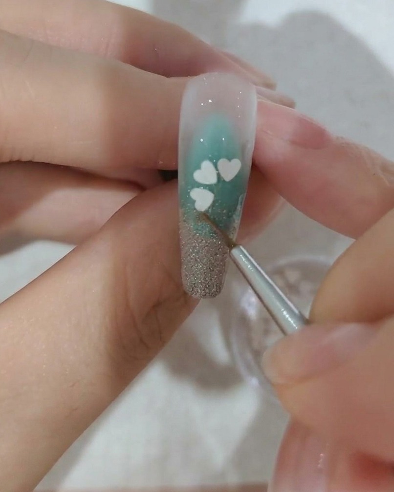 Un primo piano di ununghia decorata con una terza paillette bianca a forma di petalo di ciliegio.