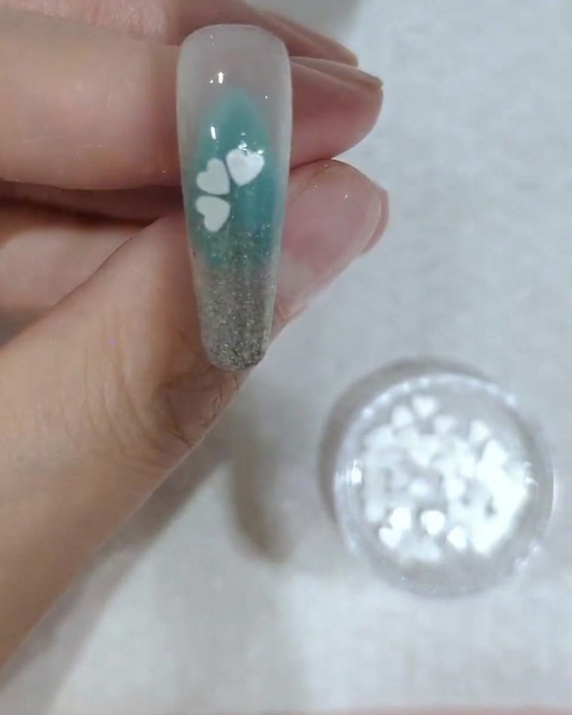 Un primo piano di ununghia che mostra il posizionamento della quarta paillette bianca a forma di petalo di ciliegio.
