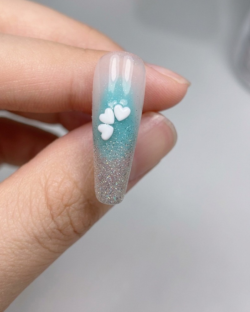 Un primo piano di ununghia con cinque paillettes bianche a forma di fiore di ciliegio disposte in un fiore completo.