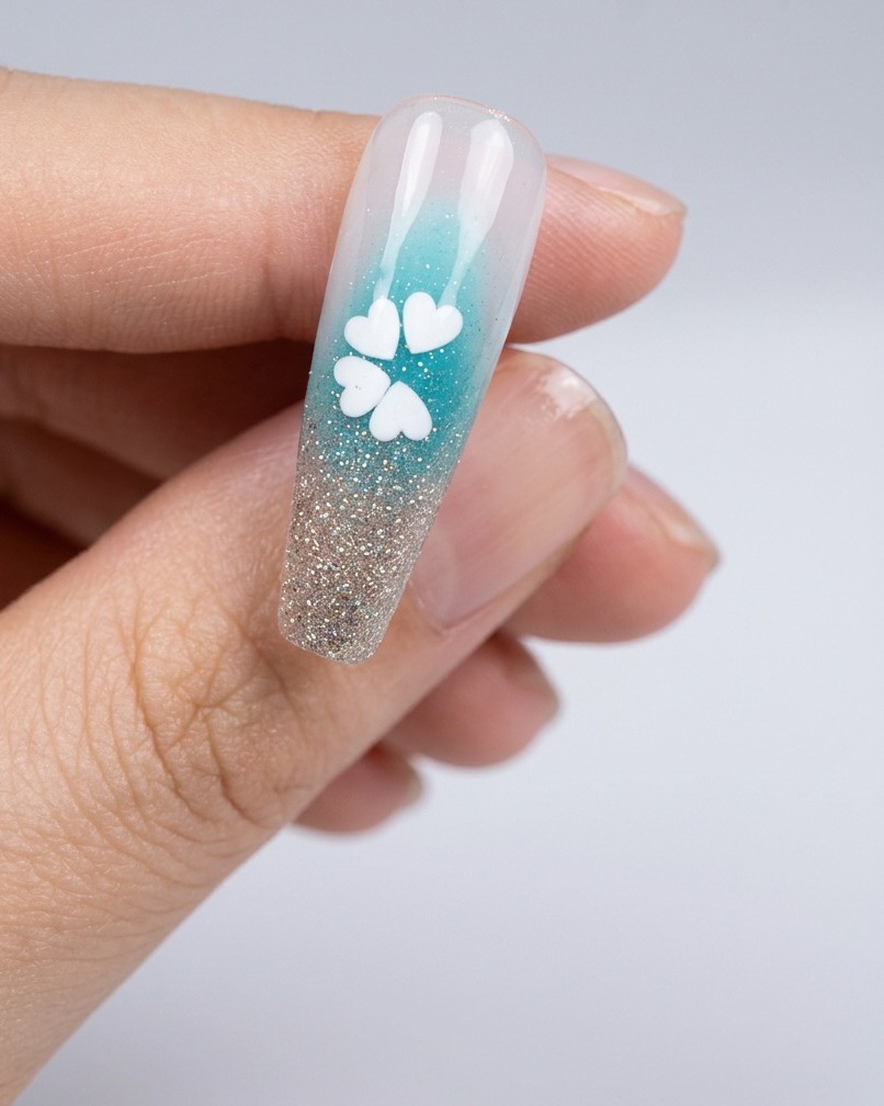 Un primo piano di ununghia con un minuscolo punto di colla posto al centro del fiore di paillettes bianco.
