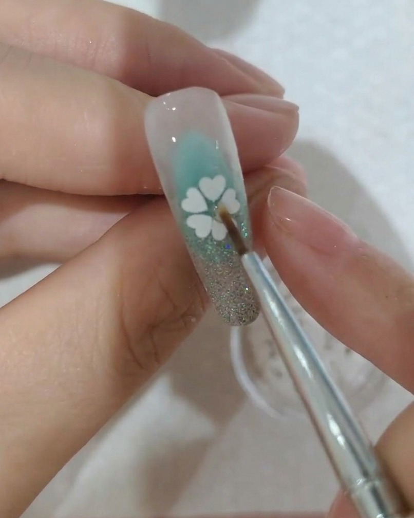 Un primo piano di un piccolo cristallo che viene posizionato al centro del fiore di paillettes su ununghia.
