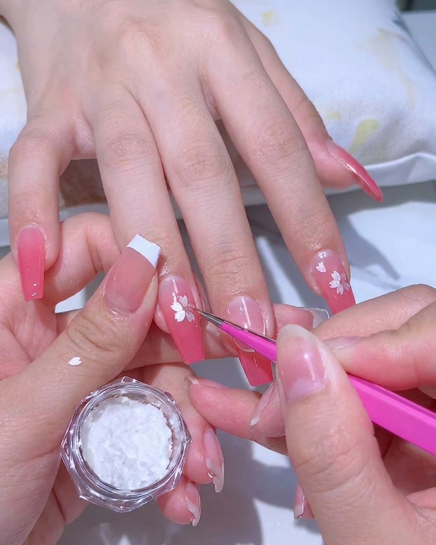Applicazione di un gel adesivo trasparente sopra una manicure con sfumatura rosa usando un pennello a punta fine.
