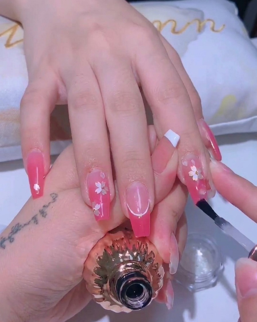 Un pennello per unghie applica un top coat sottile e lucido sopra un design di fiori di ciliegio.