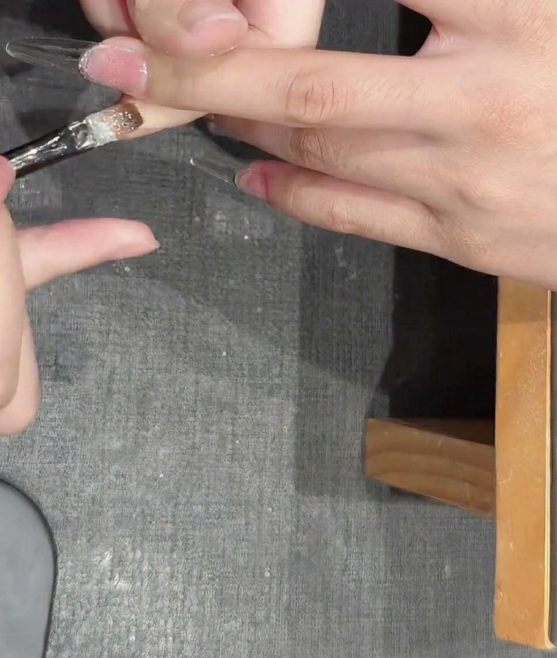 Pinzette che posizionano piccoli pezzi di glitter metallizzati a forma di stella su ununghia con gel fresco.