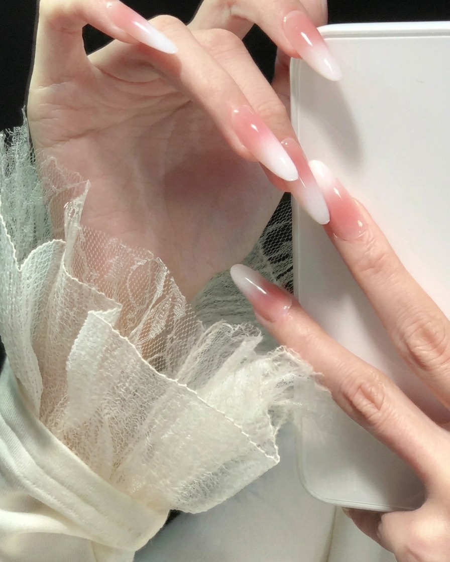 Mano con le dita aperte che mostra un aspetto ombré sfumato dal rosa al bianco coerente su tutte le lunghe unghie a mandorla.