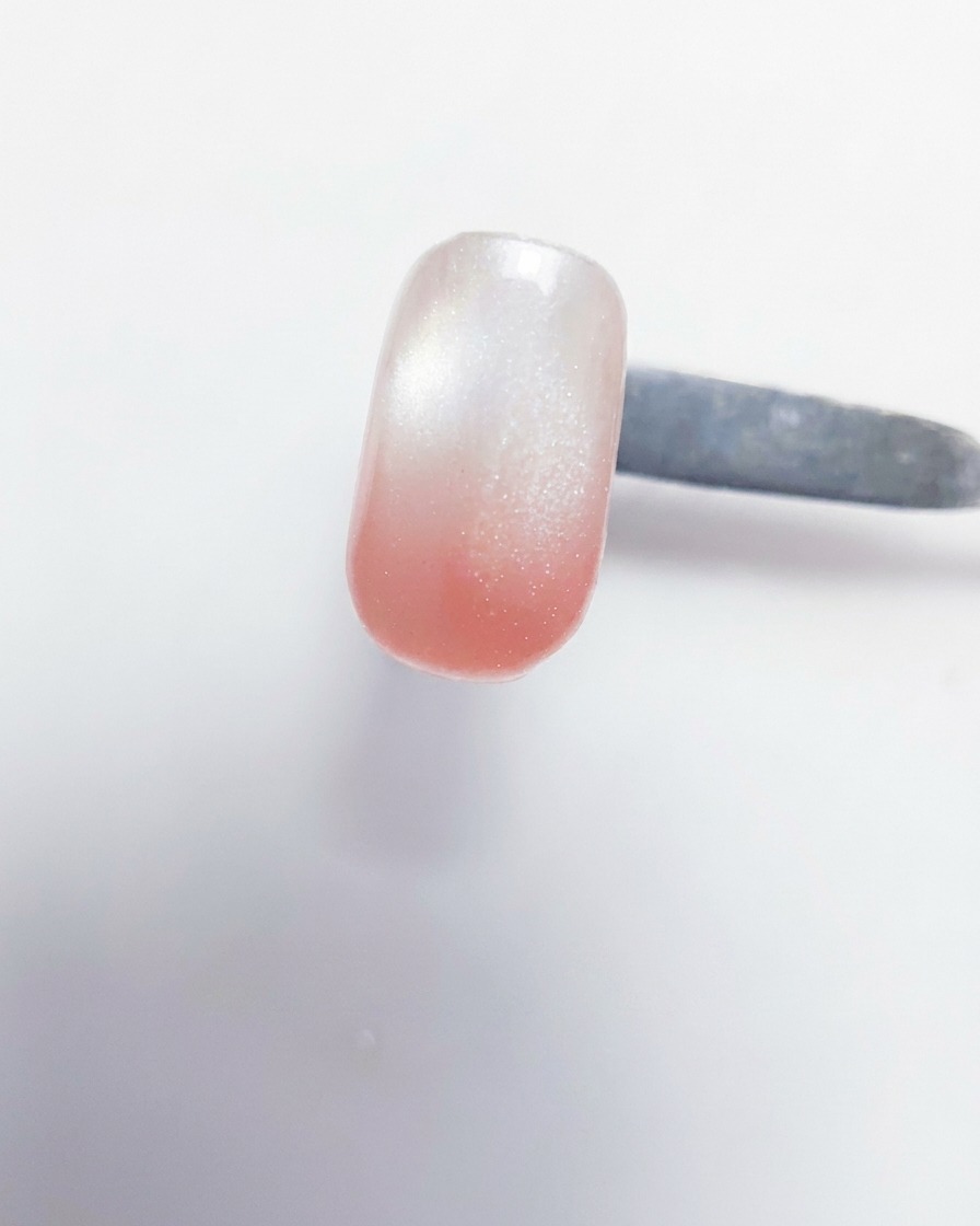 Primo piano di un pennello da gel che deposita gel color pesca-rosa sulla punta di ununghia che ha già una base bianco latte.