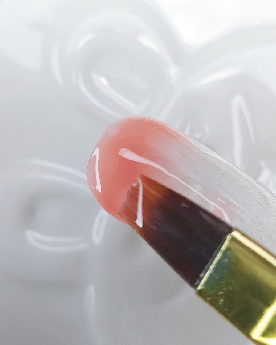 Primo piano di un pennello che trascina il gel pesca-rosa verso lalto sopra una base bianco latte per creare un effetto ombré.
