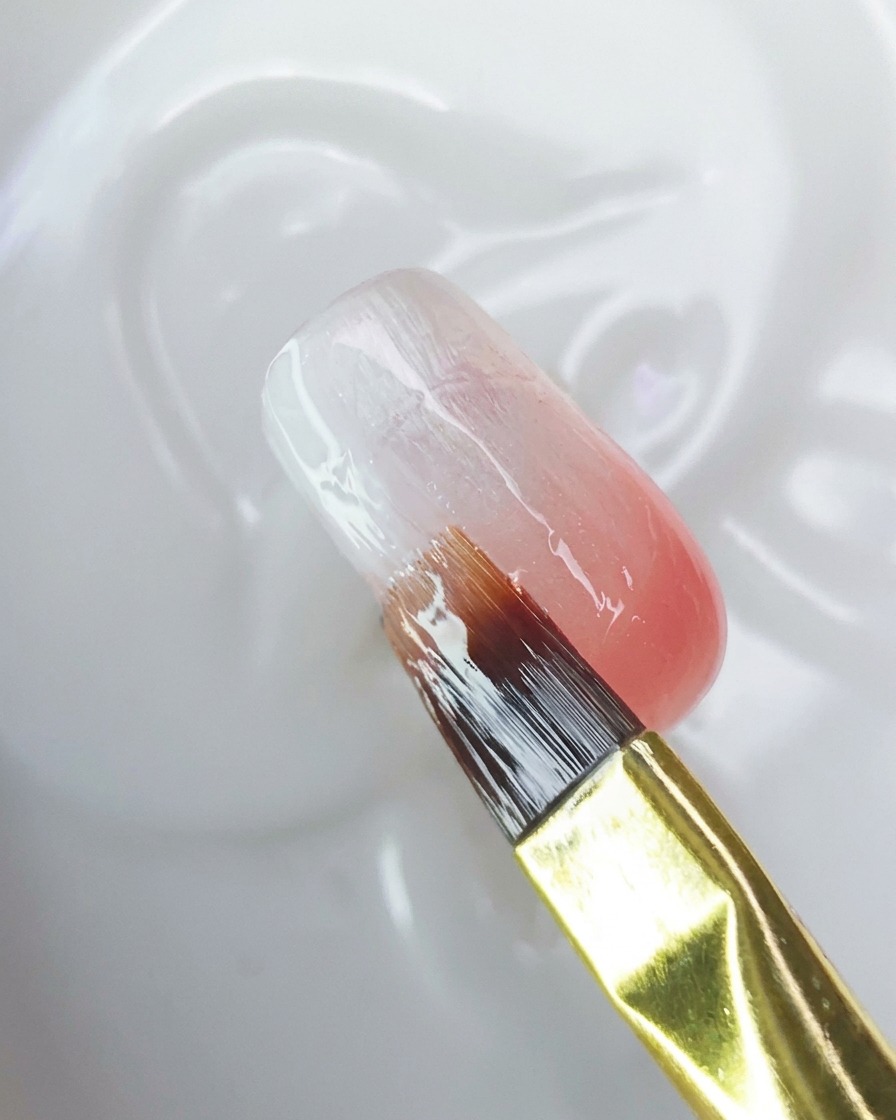 Un pennello che applica un top coat trasparente sulla superficie dellunghia sfumata.