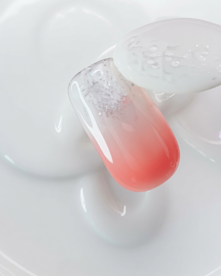 Un pennello che applica gel magnetico cat-eye trasparente sopra ununghia rivestita di polvere aurora.