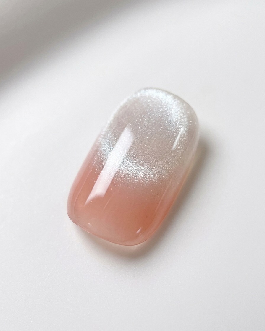 Un magnete sferico per unghie tenuto fermo sopra ununghia sfumata rosa e bianca con gel magnetico bagnato, evidenziando la formazione di una brillante striscia cat-eye.