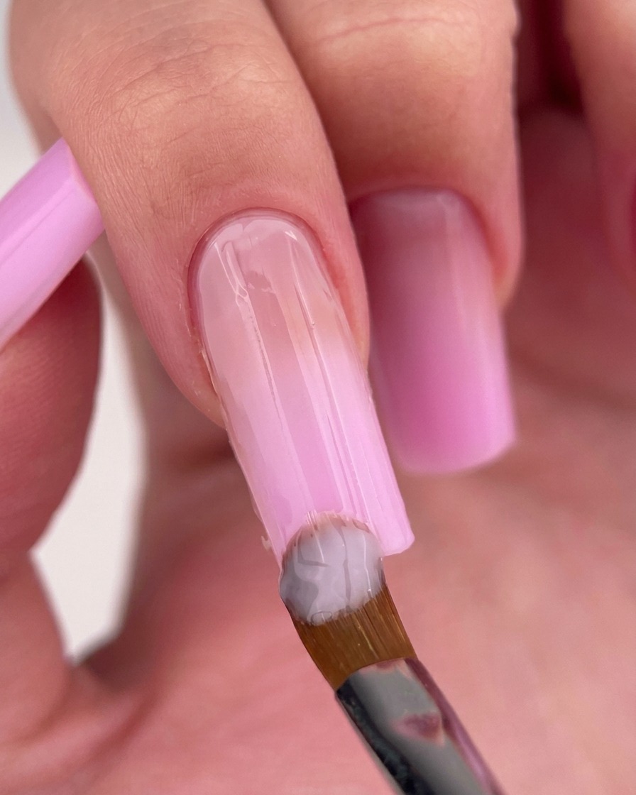 Un pennello da unghie che applica uno smalto gel rosa lattiginoso vicino alla cuticola dellunghia.