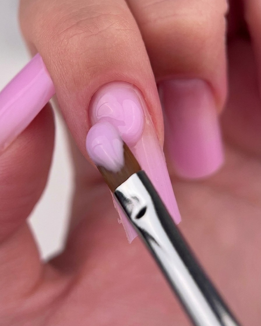Un pennello da gel pulito che sfuma delicatamente la giunzione tra due tonalità di smalto rosa su ununghia.