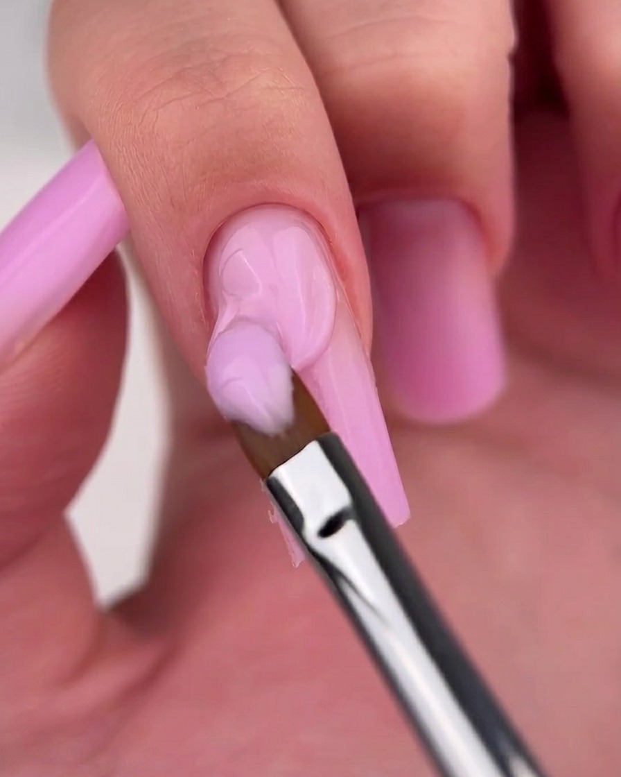 Primo piano di un pennello che uniforma la transizione sfumata su ununghia con ombré rosa.