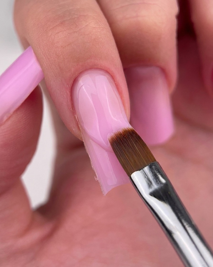 Un pennello a punta sottile che pulisce accuratamente il bordo del gel rosa sulla cuticola.