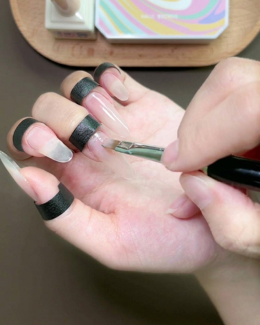 Un pennello piatto applica uno strato sottile di gel nude sullunghia del dito medio.