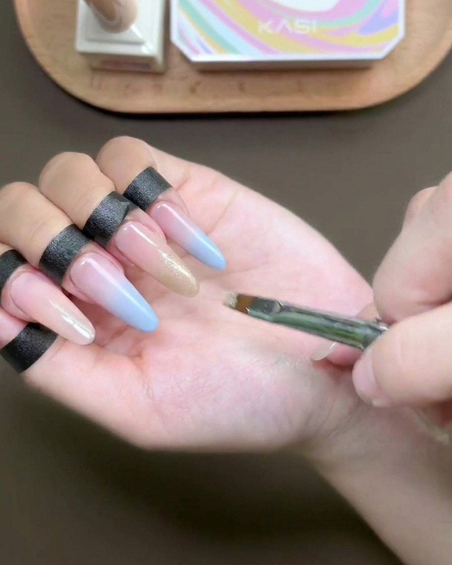 Un pennello piatto applica un gel cat-eye champagne scintillante sulla punta di ununghia.
