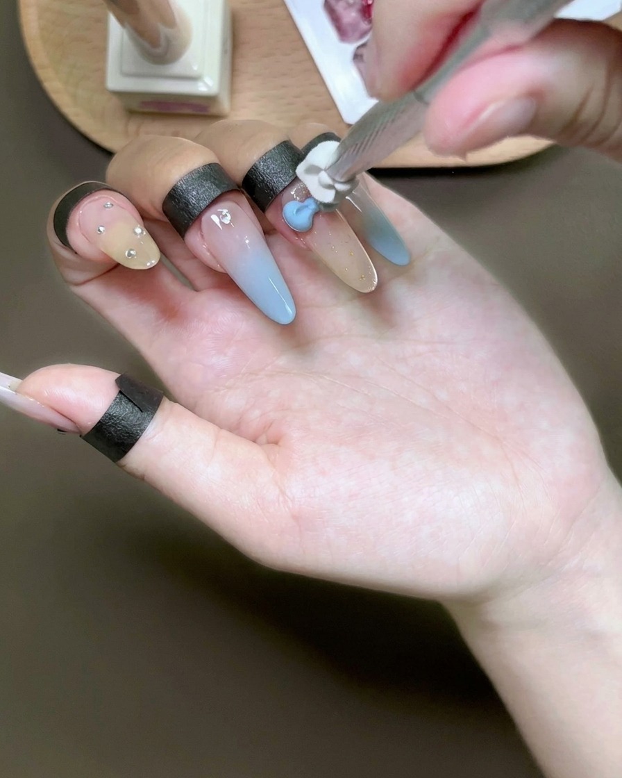 Uno strumento in spugna picchietta del gel azzurro su un ciondolo 3D a forma di fiocco bianco su ununghia.