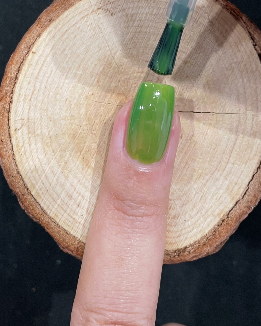 Un pennello applica meticolosamente gel verde vicino alla cuticola di ununghia.