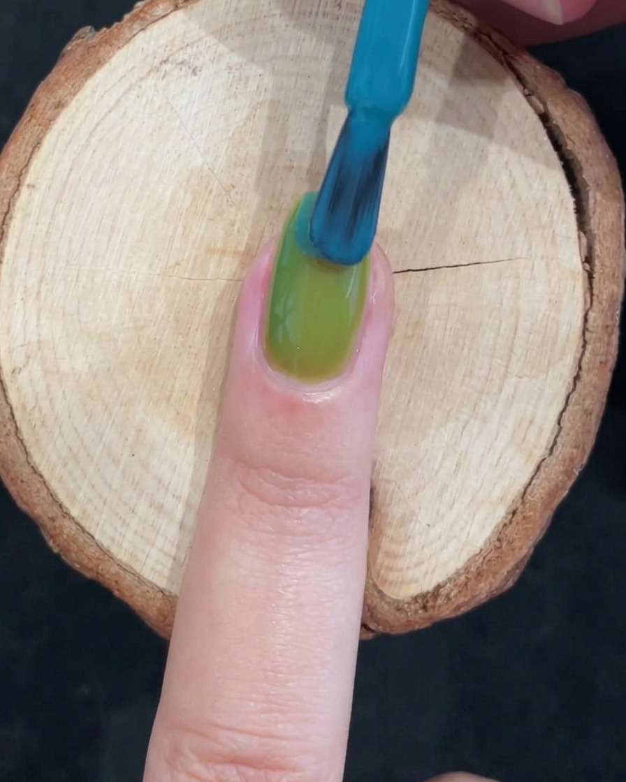 Un pennello applica gel blu vibrante sulla metà superiore di ununghia già verde per creare una sfumatura.