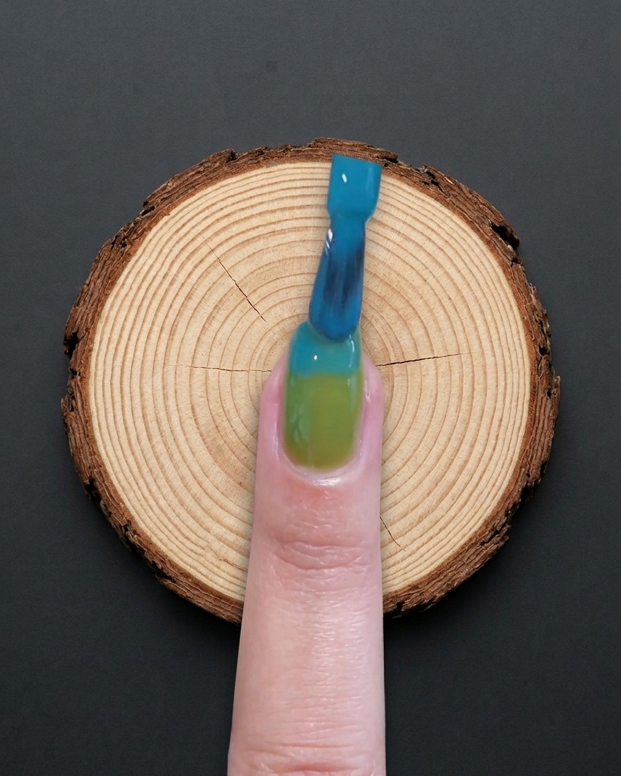 Un pennello applica gel blu sulla metà superiore di ununghia con base verde.