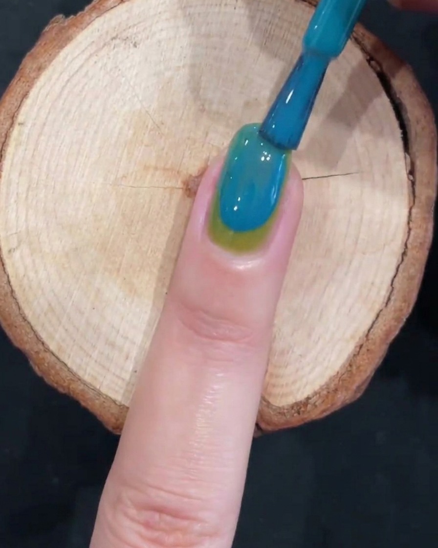 Un pennello crea un effetto gradiente liscio su ununghia bicolore verde e blu.