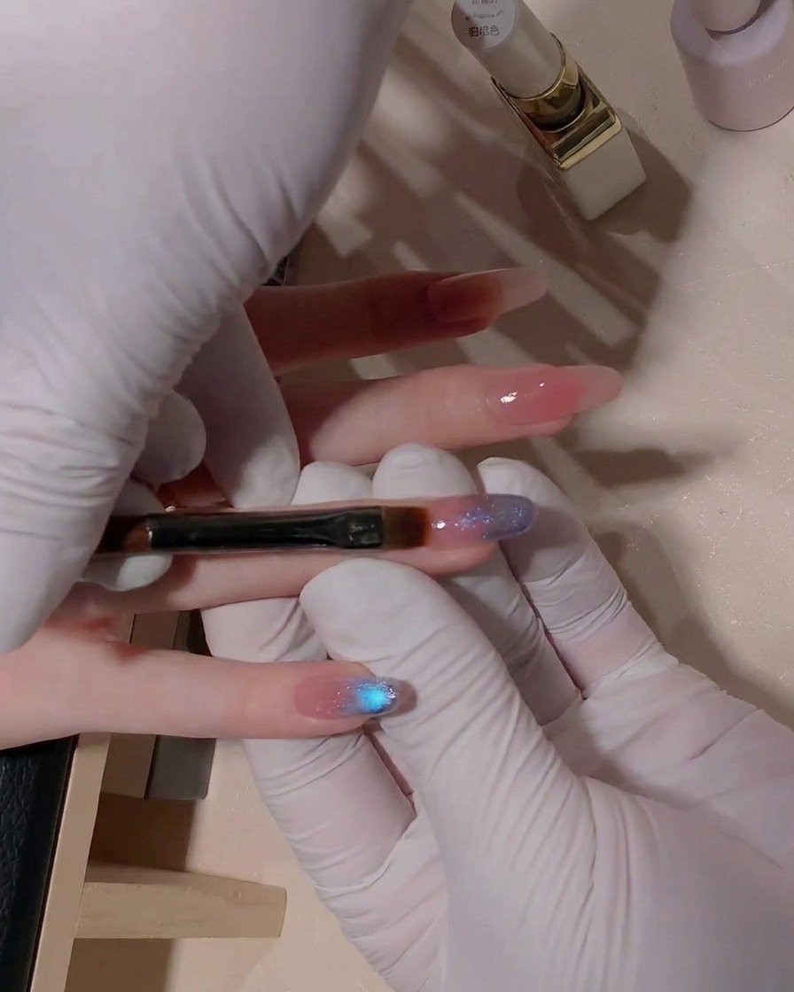 Un primo piano che mostra un pennello a punta piatta mentre sfuma delicatamente la transizione del gel cat-eye blu sulla superficie dellunghia.