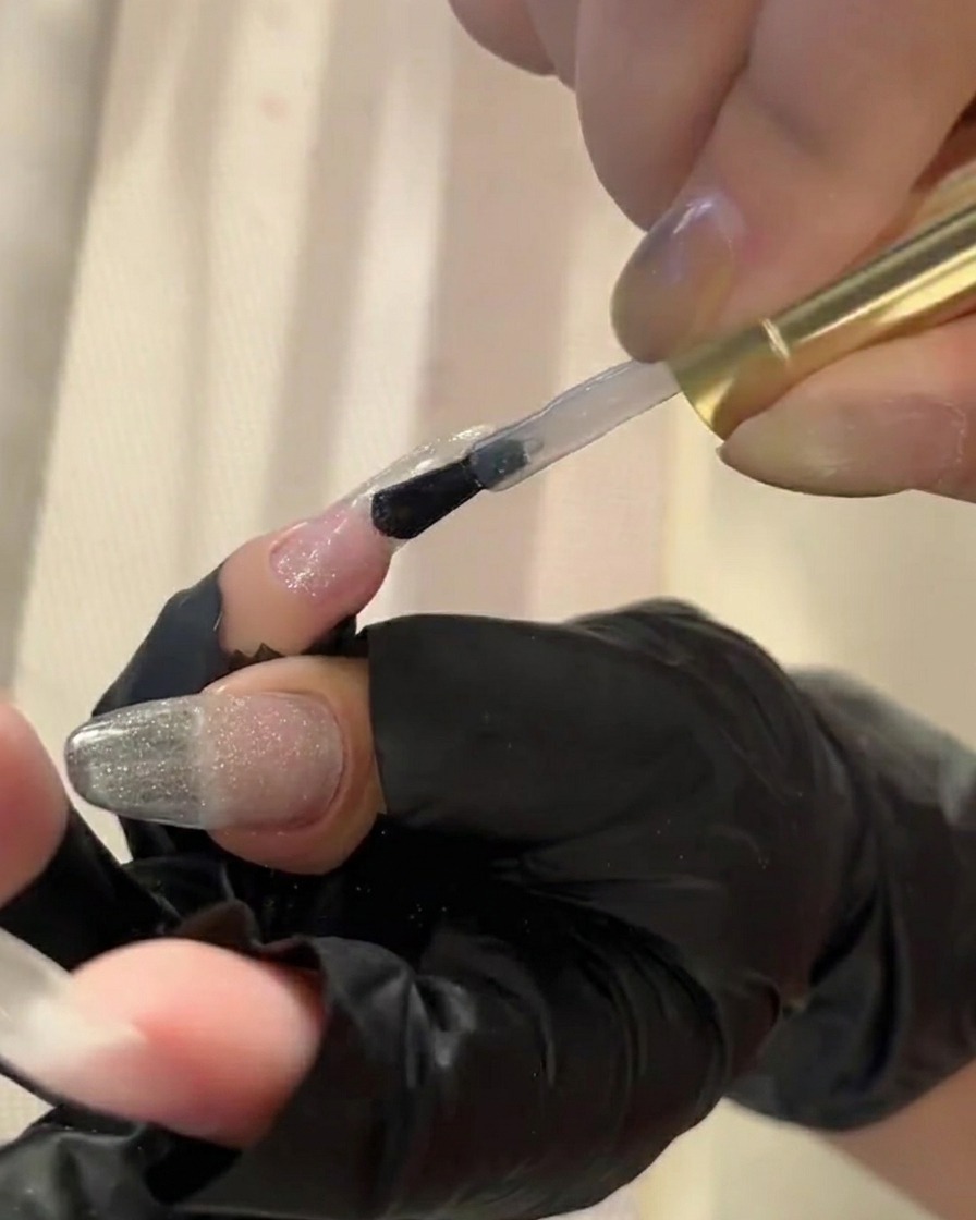 Un pennello che applica un top coat trasparente su ununghia, preparandola per lapplicazione della polvere pigmentata.