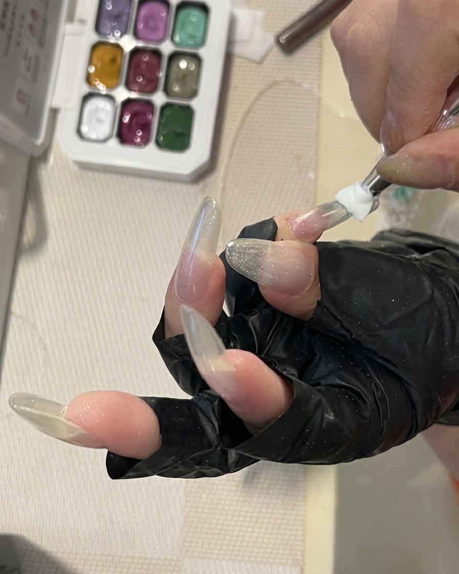 Un primo piano di un pennello per nail art che sfuma un gel color verde menta sulla superficie di ununghia lunga e strutturata per creare un delicato effetto ombré.
