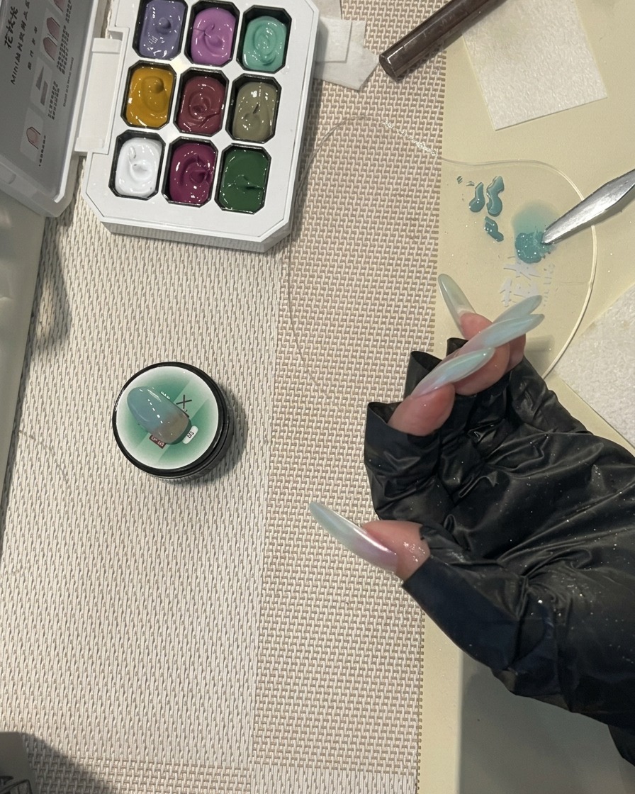 Un pennello da unghie che applica un top coat lucido finale su ununghia lunga con un design sfumato color verde menta.